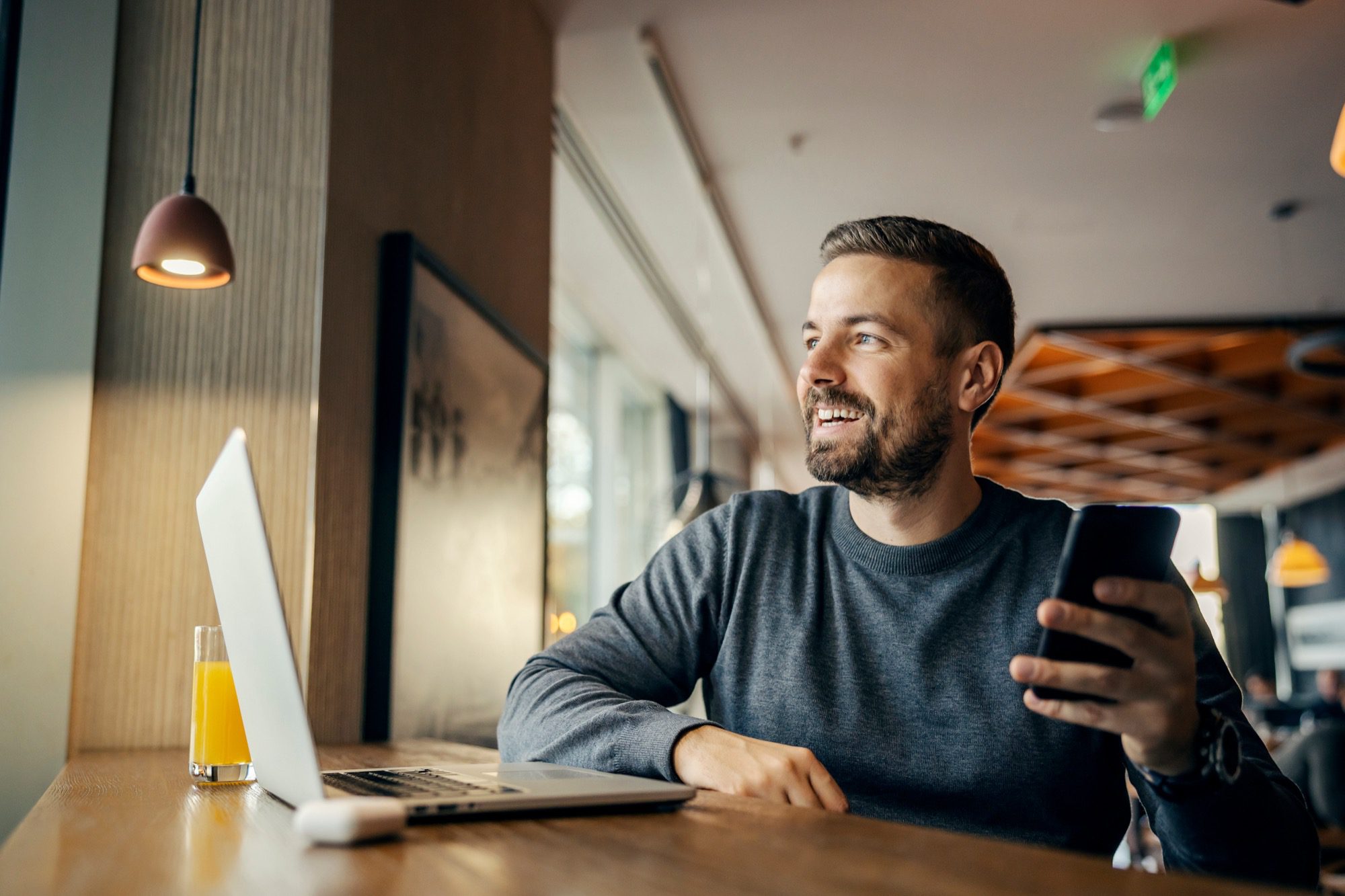 A happy casual entrepreneur is sitting in coffee shop and working on e-commerce by using cutting edge technologies.